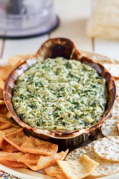 spinach dip in a bowl surrounded by crackers and tortilla chips on a plate