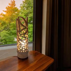 a lamp sitting on top of a wooden table next to a window with trees outside