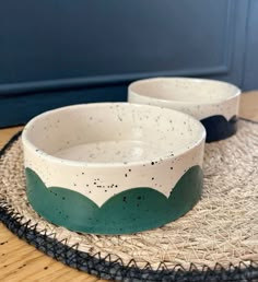 two white and green bowls sitting on top of a mat