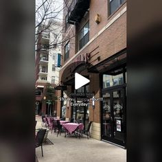 an empty sidewalk with tables and chairs in front of a building on the street corner