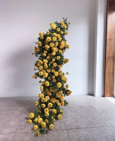 yellow flowers are arranged in the corner of a room with white walls and tile flooring