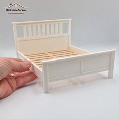 a hand holding a miniature white bed with slatted headboard and foot board