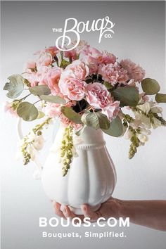 a person holding a white vase with pink flowers in it and the words bougs com