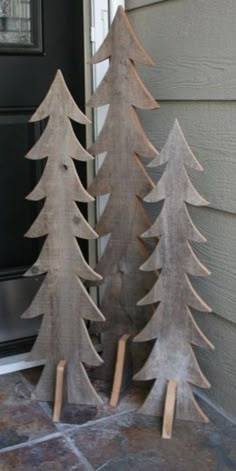 three wooden christmas trees sitting on top of a stone floor next to a door way