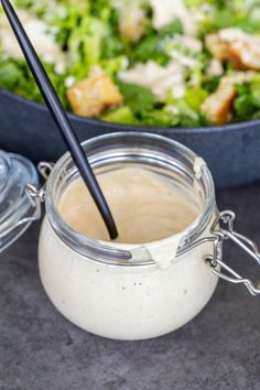 a glass jar filled with dressing next to a bowl of salad