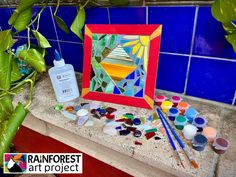 an art project with paint, brushes and paints on the counter next to a potted plant