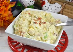 a white bowl filled with macaroni salad on top of a red plate next to flowers