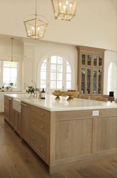 a large kitchen with wooden cabinets and white counter tops, along with two chandeliers hanging from the ceiling