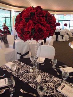 a vase filled with red flowers sitting on top of a table covered in white linens