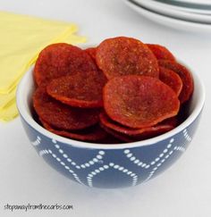 a blue and white bowl filled with red hot dogs next to a yellow napkin on top of a table