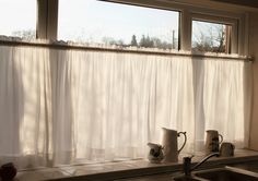 two mugs are sitting on the windowsill in front of a window with white curtains