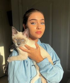 a woman holding a cat in her arms and looking at the camera with an intense look on her face