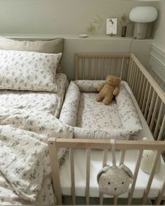 a baby crib with a teddy bear in it and pillows on the bottom bed