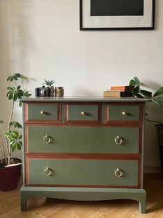 an old dresser painted green and brown with brass pulls in front of a potted plant