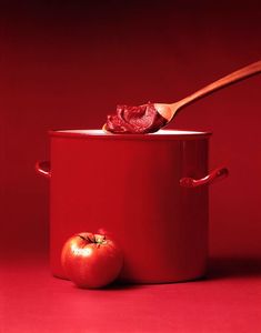 a red pot with two tomatoes and a wooden spoon