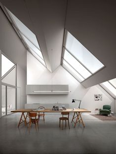 an empty room with two wooden chairs and a table in it, under a slanted ceiling