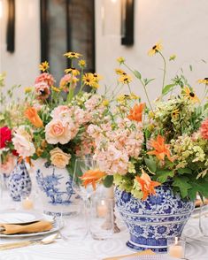 an arrangement of flowers in blue and white vases on a table with place settings