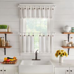 a white kitchen with sunflowers and fruit on the counter next to the window