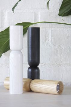 three black and white vases sitting on top of a table next to a plant