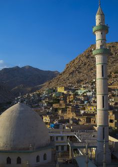 a tall white building with a green dome on top of it's roof and mountains in the background