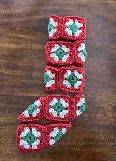 three crocheted red and green squares with white flowers on them sitting on a wooden surface