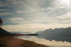 the sun shines brightly over a lake with mountains in the background