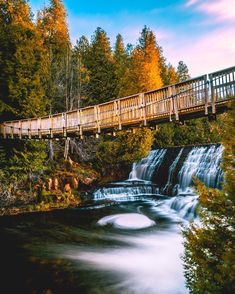 a wooden bridge over a river next to a waterfall