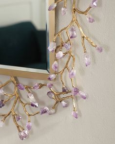 a mirror mounted to the side of a wall next to a branch with purple stones