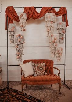 an orange chair sitting in front of a white wall with red drapes and tassels hanging from it