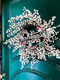 a green door with a christmas wreath on it and the words'christmas is coming'written in white letters