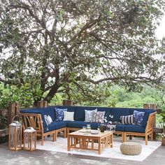 an outdoor living area with blue couches and pillows on the floor under a tree