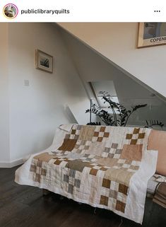 a couch with a quilt on it sitting under a stair case