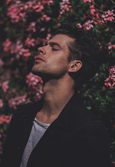 a man is standing in front of some pink flowers and looking up at the sky