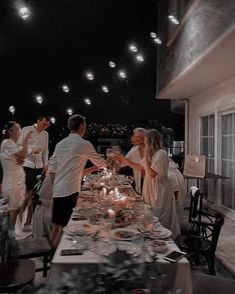 a group of people standing around a table with food and drinks on it at night