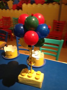 there is a lego table with balloons on it and some chairs in the back ground