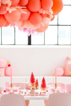 the table is set for a party with pink decorations and balloons hanging from the ceiling