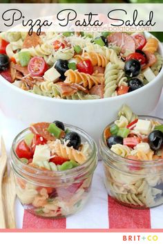 pasta salad with tomatoes, olives, and other vegetables in small glass containers on a red and white striped tablecloth