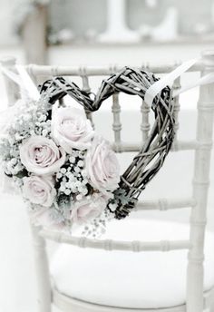 a heart - shaped wreath with pink roses is placed on the back of a chair