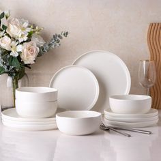 white dishes and cups on a table with flowers in the vase next to each other