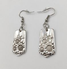 two silver earrings with flowers and dragon design on the front, one is dangling from hooks