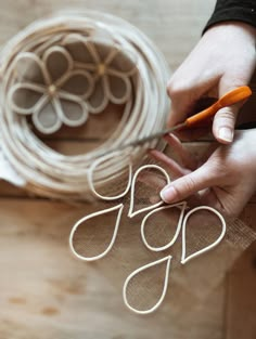 a person cutting paper with scissors on top of a piece of wood next to some wire