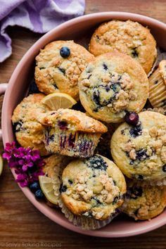 blueberry muffins in a pink bowl with lemon wedges and purple flowers