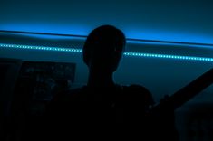 a man holding a bat in the dark with blue light coming from behind him and his shadow on the wall