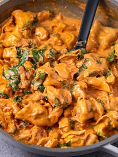 a skillet filled with pasta and spinach covered in sauce, garnished with parsley