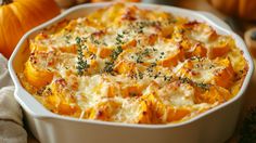 a casserole dish with cheese and herbs in it on a table next to pumpkins