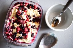 a bowl of food with berries and cream in it next to a spoon on a table