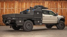 a large truck parked in front of a wooden building next to a tall brown wall