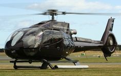 a black helicopter sitting on top of an airport tarmac next to a field with grass