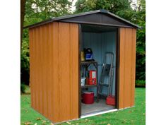 a wooden shed with its doors open in the grass and trees behind it, next to some trash cans