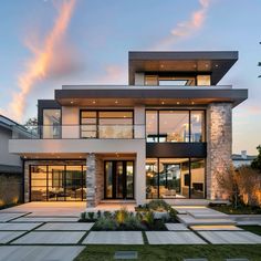 a large modern house with lots of windows and grass in the front yard at dusk